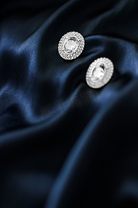 丝绸珠宝摄影照片_深蓝色丝绸背景的豪华钻石耳环，节日魅力珠宝礼物