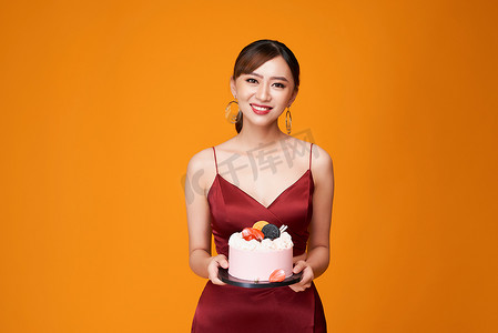 一位身穿红裙、端着生日蛋糕的优雅女性的垂直照片