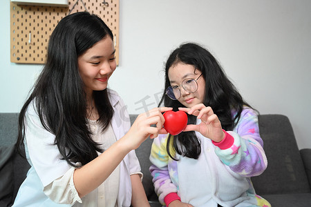 和你一起玩摄影照片_微笑的亚洲女孩穿着医疗制服假装是医生在家里和她的妹妹一起玩。