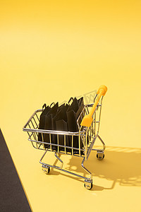 黄色背景黑色星期五销售中带购物袋的微型超市推车