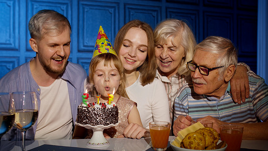 与父母庆祝生日聚会的女孩，年长的祖父母家人吹灭蛋糕上的蜡烛