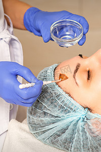年轻的白人妇女在美容诊所用刷子获取酸性有机视黄醇剥离面部皮肤。