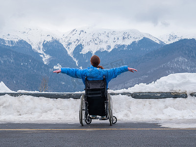 坐在轮椅上的女人的后视图在冬天的山中像翅膀一样张开双臂。