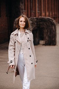 灰色外套摄影照片_一个穿着灰色外套的快乐时尚女孩在城市里走来走去