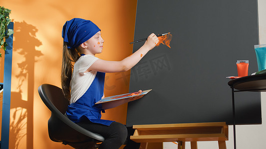 孩子在创作摄影照片_年轻的孩子在画布上用橙色绘画艺术品