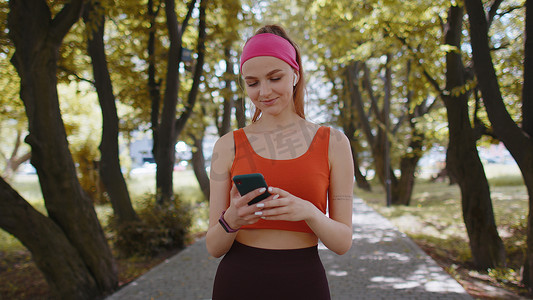 运动健身运动员女孩散步，在公园里用智能手机用耳机听音乐