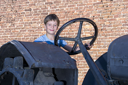 拖拉机的人摄影照片_砖墙背景中驾驶旧式拖拉机的男孩