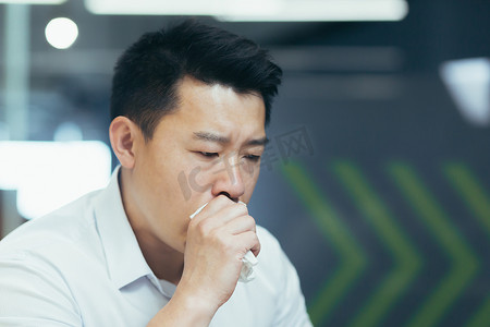 一名身穿衬衫的亚洲男子的特写照片，一名生病的商人用纸巾咳嗽