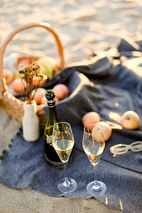 专注于一瓶香槟和眼镜，格子上放着水果的篮子，背景模糊的海滩。