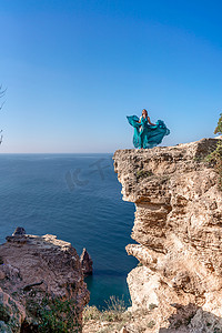一位头发松散、穿着薄荷色长裙的女孩从黄色岩石之间的楼梯上走下来，俯瞰着大海。