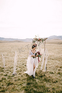 戴着花圈的新娘带着一束鲜花走在婚礼拱门附近