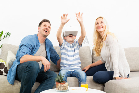 父母玩游戏摄影照片_快乐的家庭在家里的客厅沙发上使用虚拟现实耳机玩游戏