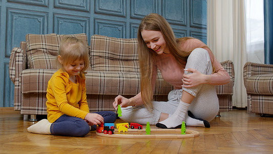 有小女儿的妈妈在家里玩木制铁路积木棋盘游戏的玩具火车