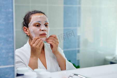 多民族美女在浴室里一边看着镜子，一边在脸上涂抹保湿平滑纸巾