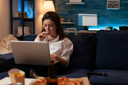 外卖零食摄影照片_在电视上看连续剧的同时吃薯片零食的女性在笔记本电脑上工作