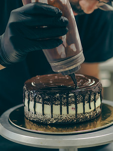 厨师蛋糕装饰师将装有巧克力甘纳许的瓶子挤在蛋糕上