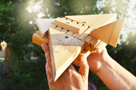 在夏日的树木、光线和阳光的背景下，一个男人的手拿着一架自制的木制玩具飞机的特写镜头。