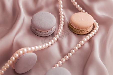 丝绸珠宝摄影照片_丝绸背景上的甜马卡龙和珍珠首饰、巴黎别致珠宝、法式甜点食品和豪华糖果品牌的蛋糕马卡龙、节日礼物