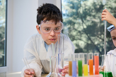 戴着护目镜的好奇男学生在化学课上观察试管中发生的化学反应