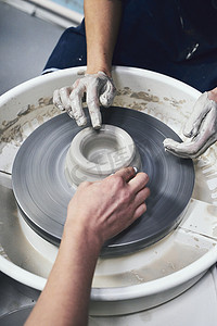 陶器摄影照片_女人在轮子上制作陶瓷陶器，手特写。