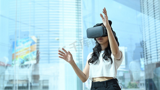 界面交互摄影照片_戴着虚拟现实眼镜的创意女性开发人员，站在现代办公室的大窗户附近，与数字界面进行交互。