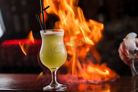 酒保在吧台上洒上带亮绿色冷鸡尾酒的照明玻璃，并在上面点燃火焰