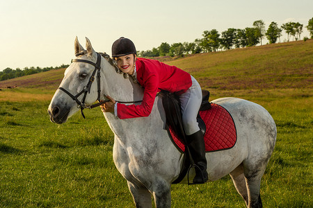 年轻的女骑手，穿着红色的 redingote 和白色的马裤，她的马在夕阳的余晖下。