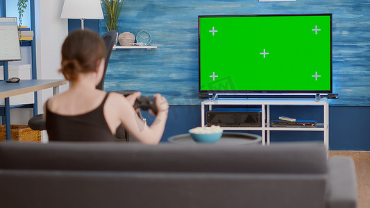 游戏玩家女孩手持无线游戏板在绿屏电视上玩动作控制台视频游戏的静态三脚架镜头