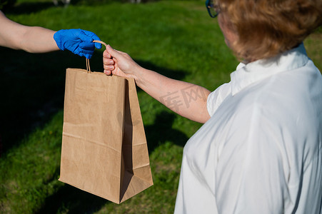 戴着手套的女快递员将食品包裹带给退休的老妇人。