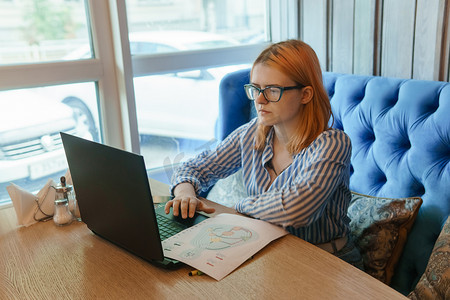 俄罗斯特维尔 — 2021 年 8 月 2 日。咖啡馆里，一位女士坐在桌子旁，手里拿着笔记本电脑正在研究人的设计。
