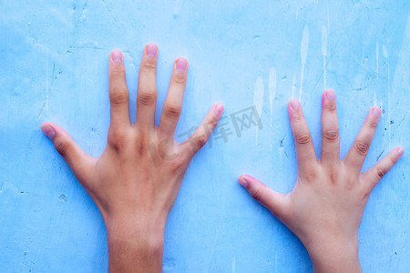 两只人类的手，一只是男性，另一只是女性，在蓝色背景上，与两个不同个体的大小形成鲜明对比。