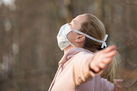 在森林里深呼吸放松时戴着医疗防护面罩的白种运动女性的画像。