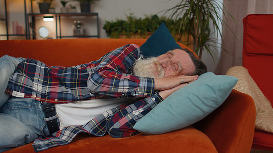 一位疲惫的老人躺在床上在家休息，打瞌睡，在沙发上睡着了