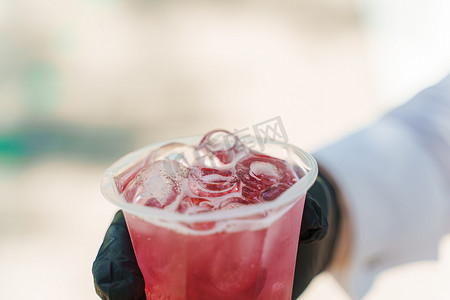 塑料杯中装有冰块的红柠檬水，特写在戴着黑手套的侍者手中