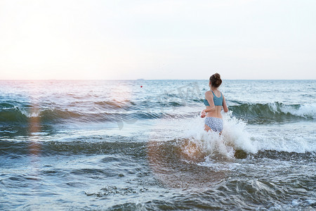 红色海浪摄影照片_穿着泳装的女孩正在沙滩上玩海浪-跳跃、奔跑、玩乐。