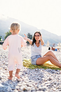 打开双臂人摄影照片_小女孩沿着海滩走向她的母亲，张开双臂