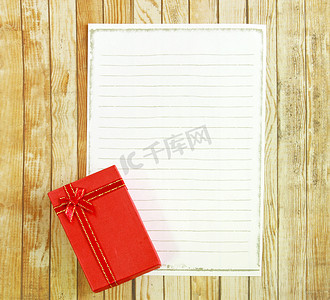 礼物盒制作摄影照片_木制背景上有空白便条纸的红色礼物盒