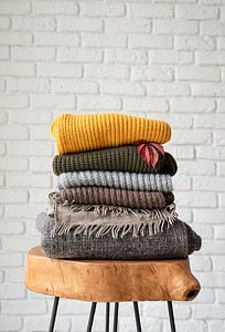 毛织品摄影照片_现代咖啡桌上堆放着秋季温暖的毛衣，白砖墙背景