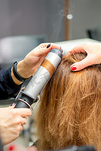 女发型师的手在美发沙龙里用卷发器给顾客卷发，特写。