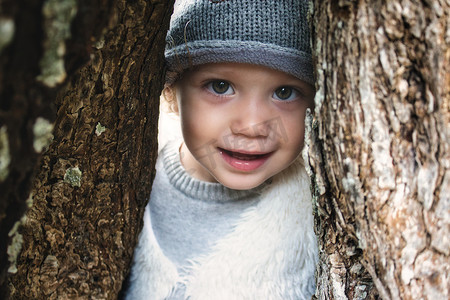 穿着冬装的美丽少女模特微笑着透过树林中树干之间的缝隙凝视