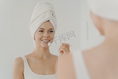 淋浴后头戴毛巾的健康美女，一边轻轻刷牙，一边露齿微笑