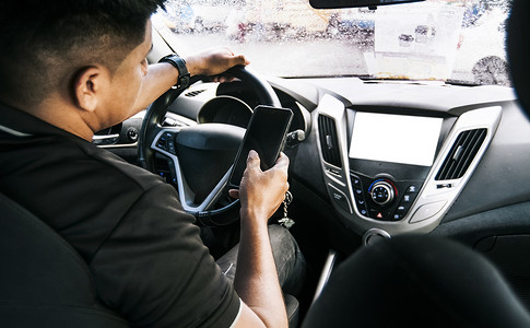 智能驾驶车摄影照片_手持手机，另一只手握方向盘的人，驾驶时使用手机的分心驾驶员，驾驶时使用手机的人，不负责任驾驶的概念