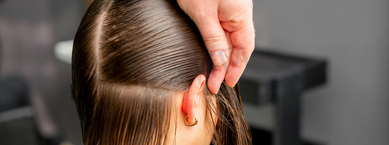 美发师将女性头发分成几部分，用梳子在美发沙龙特写中用手握住头发。