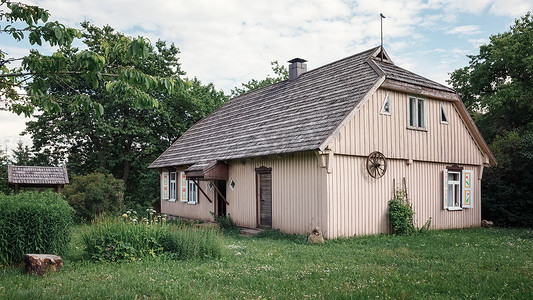 立陶宛普拉特利亚伊，古老、废弃的米色农舍，有树木、草地、蓝天，墙上有马车轮。