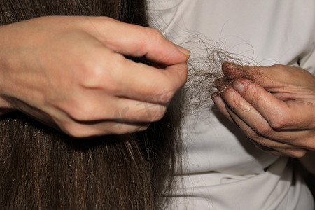 损失摄影照片_一个有着长长的黑发的女孩手里拿着一束掉落的头发。