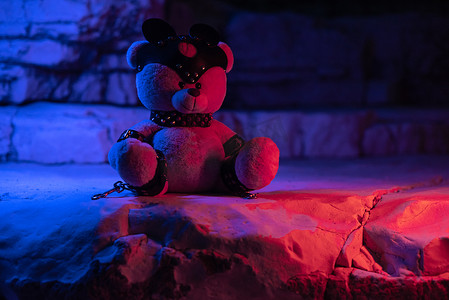 岩石背景中霓虹灯下的泰迪熊上的 bdsm 配件