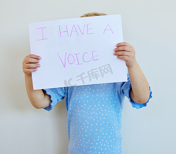反对家庭暴力海报摄影照片_小女孩举着牌子抗议家庭暴力和强奸儿童。