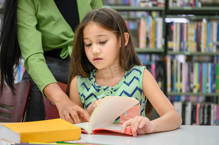 幼儿园图书馆摄影照片_女孩在学校图书馆看书时要求老师回答书中的问题。