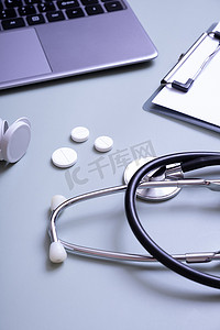 听诊器，在笔记本电脑和平板电脑的背景下，桌面上有容器的药丸