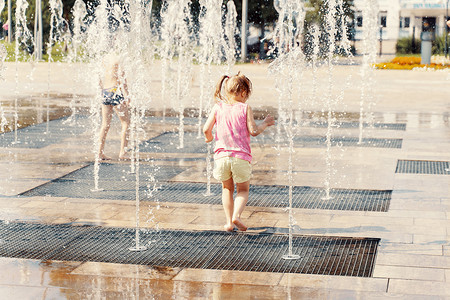 溪流玩耍摄影照片_小女孩在喷泉的水射流中玩耍